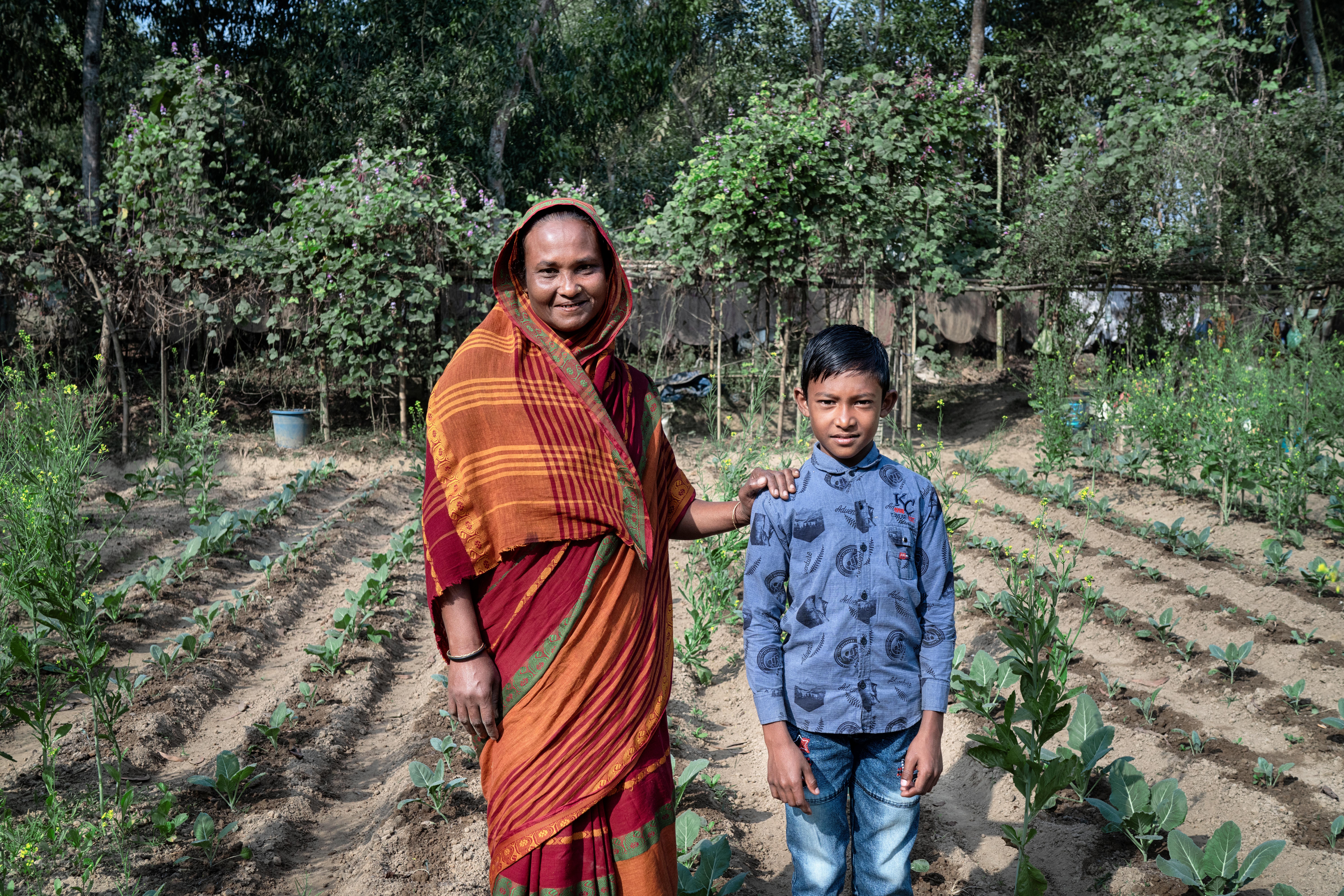 CH1771734_Rashel, 10, and his mum Rashida, 40, smiling by their vegetable farm in Sylhet, Bangladesh