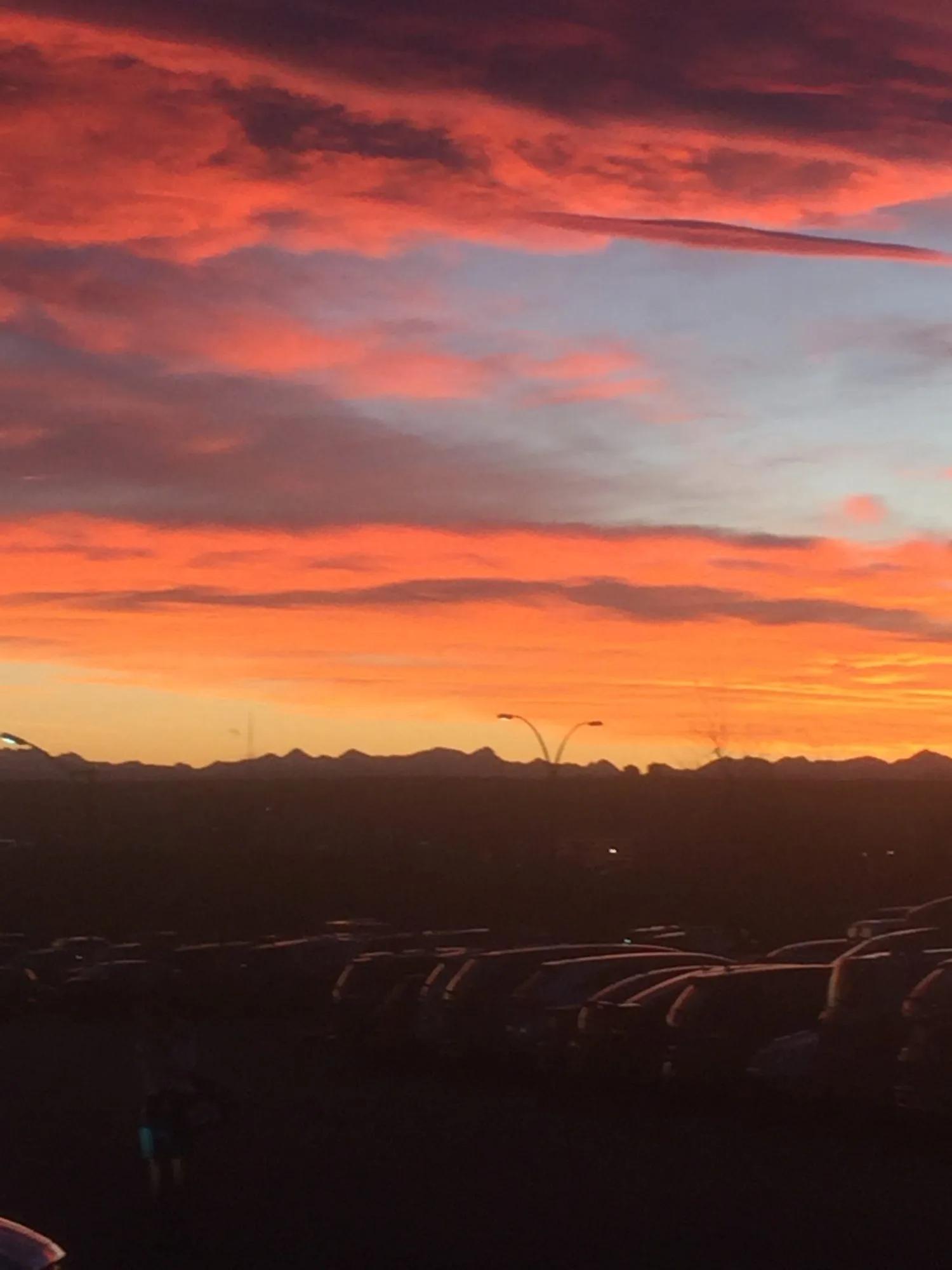 Vibrant orange, pink, and purple sunset clouds stretching across the sky above silhouetted vehicles and a distant horizon.