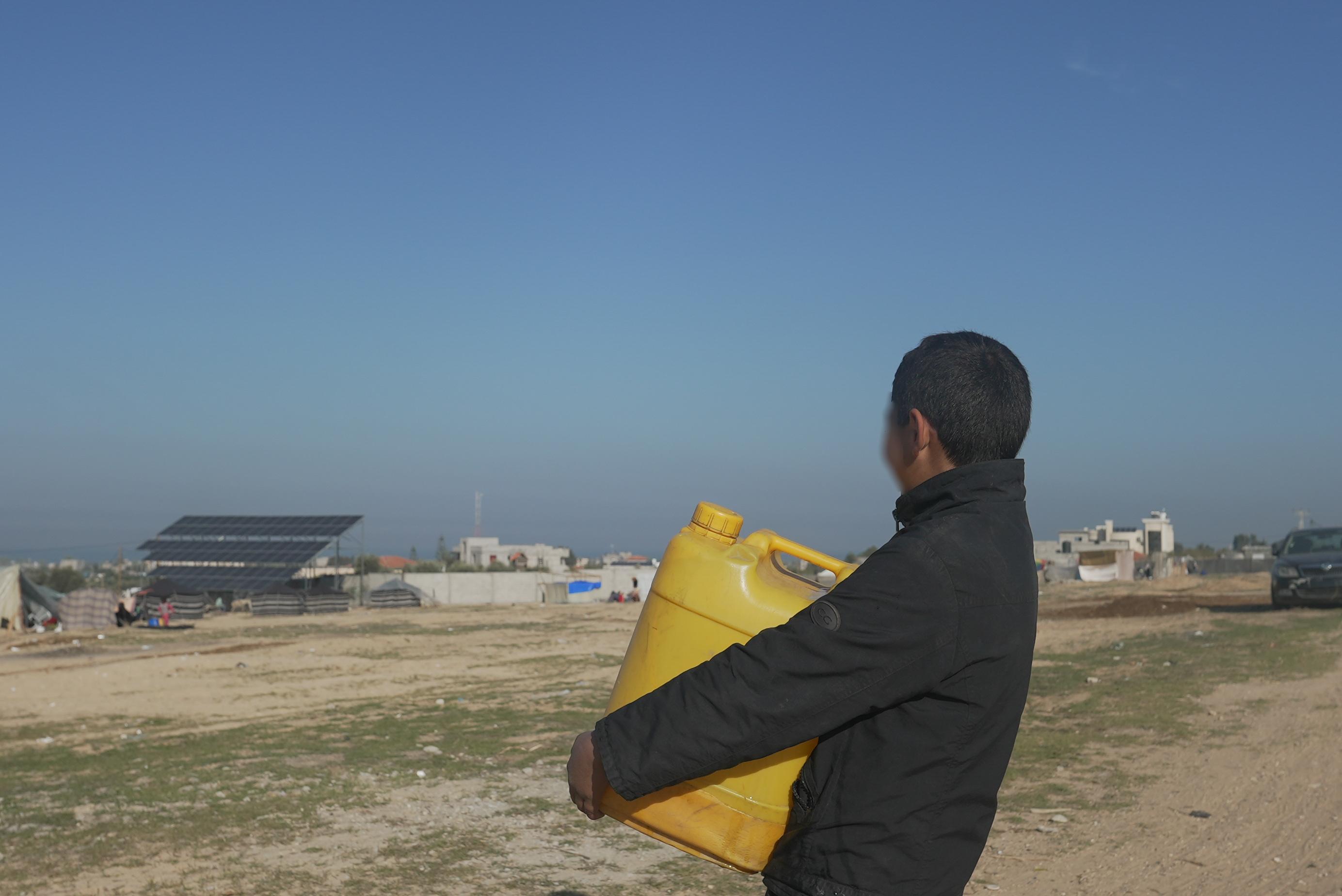 Boy carrying a jerrycan of water past makeshift tents