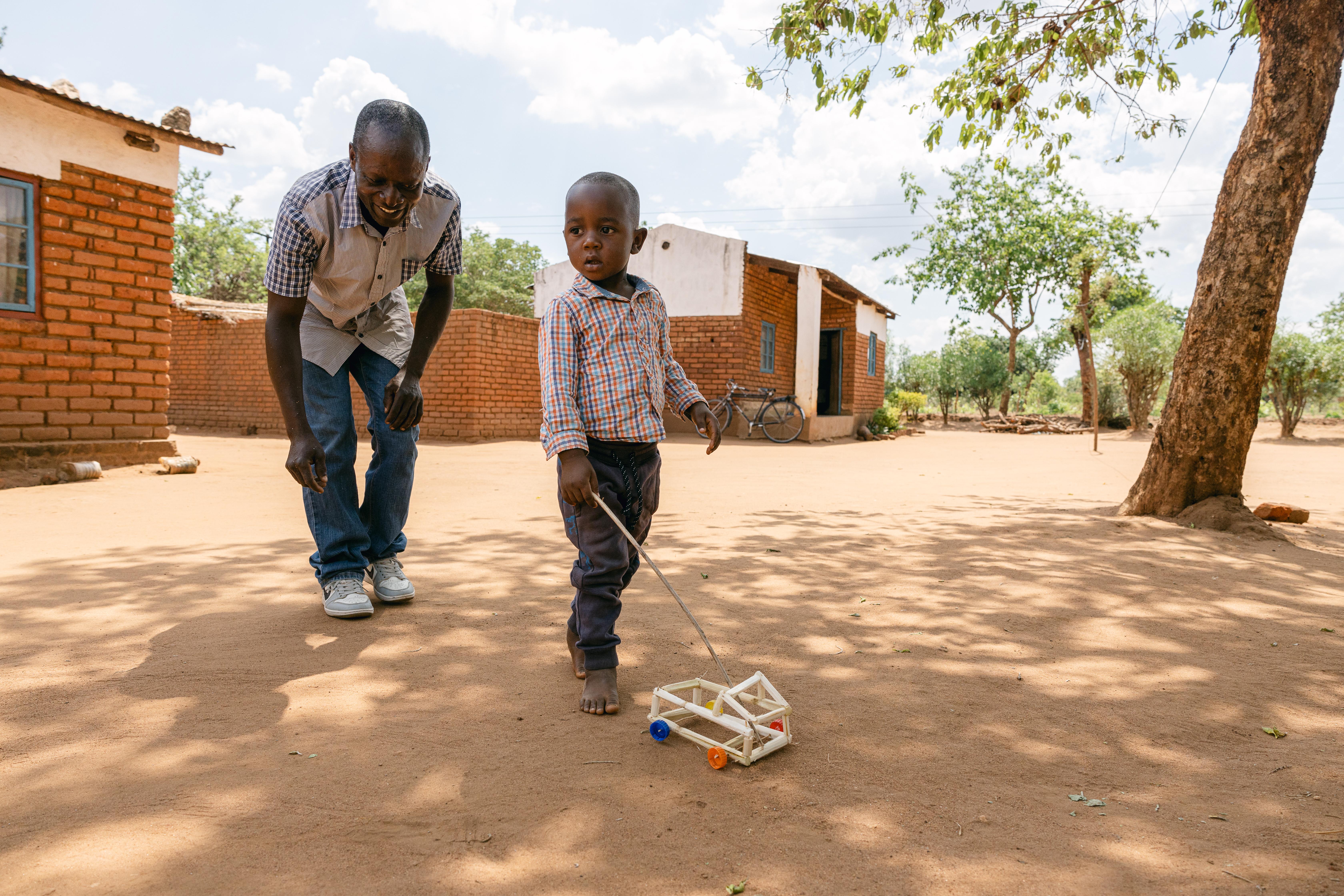 'Male Champion' Rhodrick, makes a toy for his son, Maclean, three, at their home in Balaka district, Malawi.