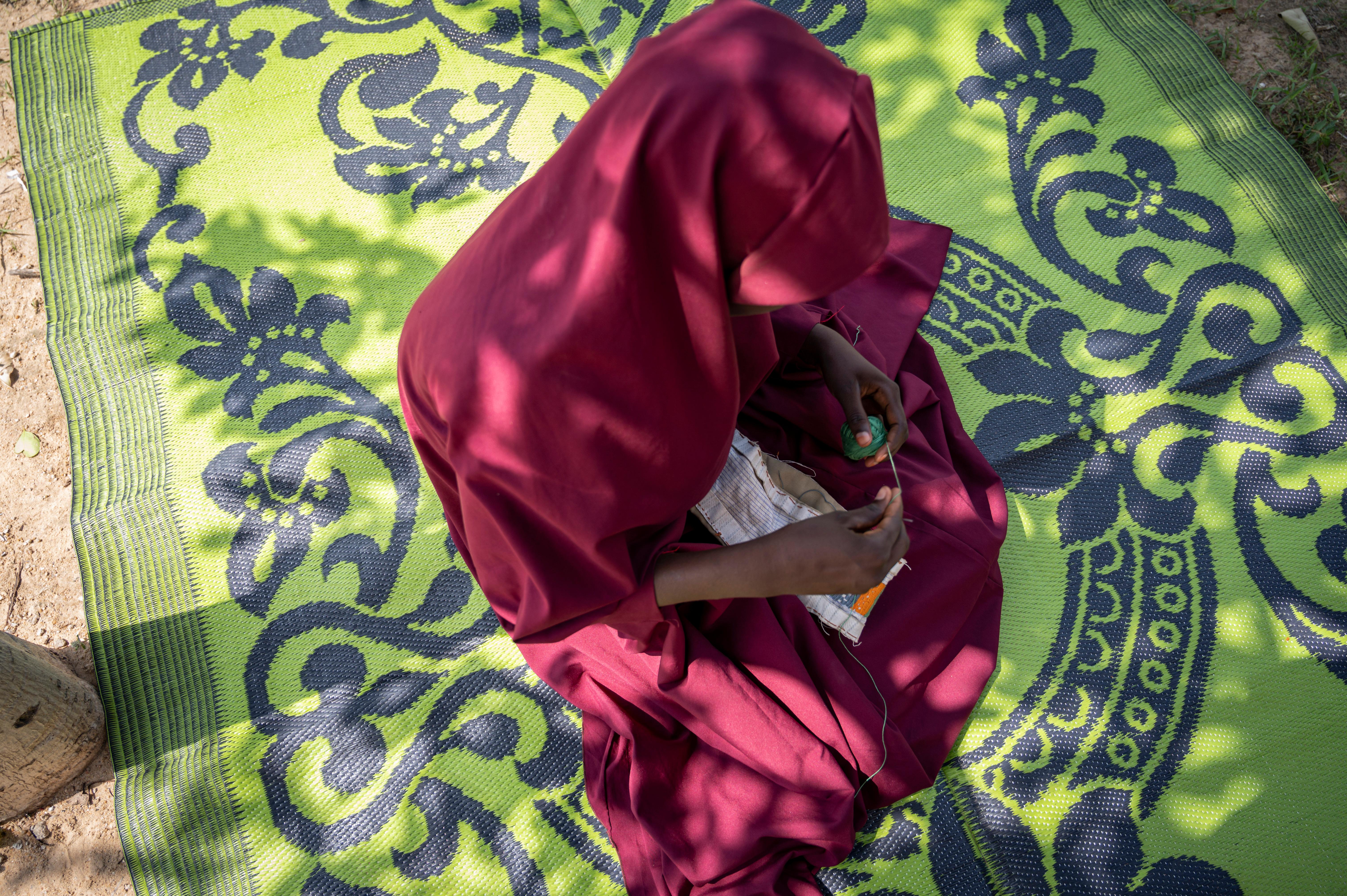 Zara* sewing outside her home in Borno, Nigeria