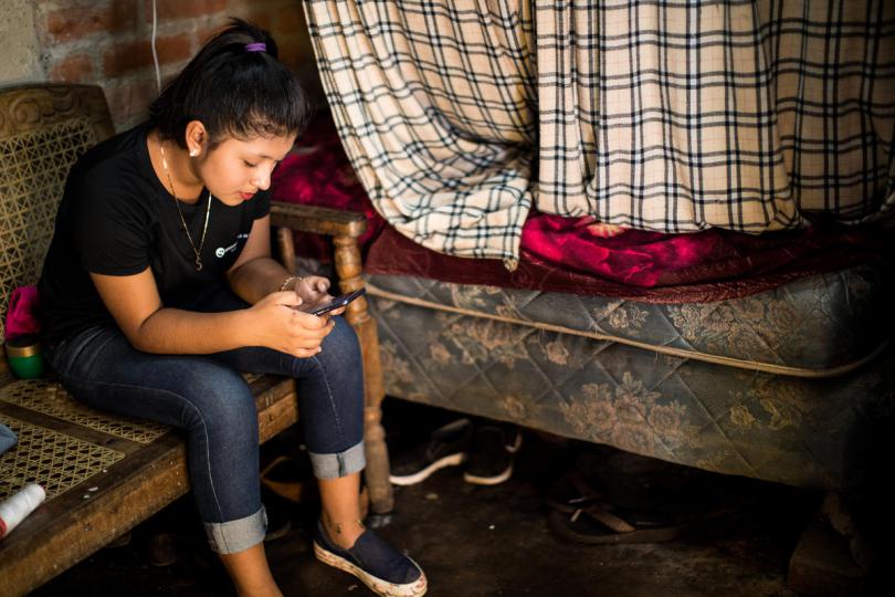 Alejandra*, 15, plays on her mobile phone inside her bedroom in El Salvador.