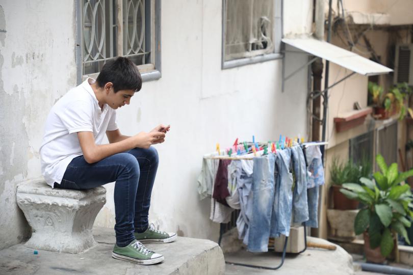 Jad*, 14, plays on his phone outside his home in Beirut, Lebanon