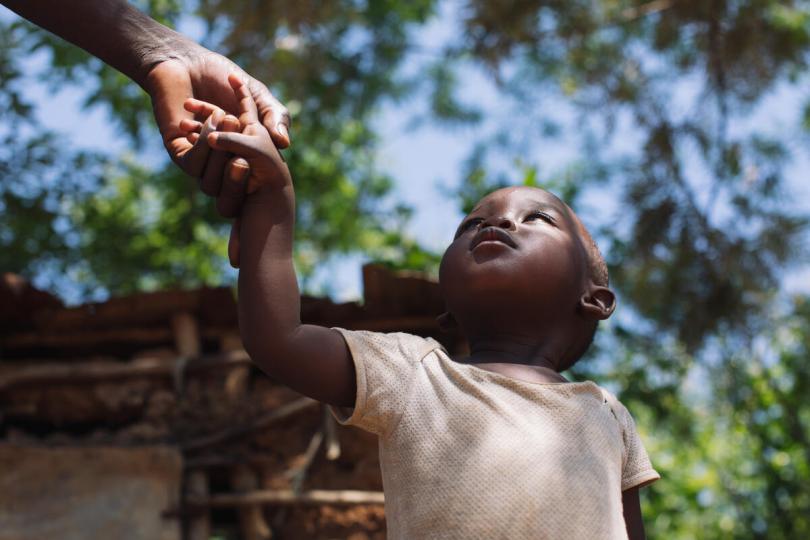 Joseph, 2, holds his father's hand outside their home in Bungoma, Kenya
