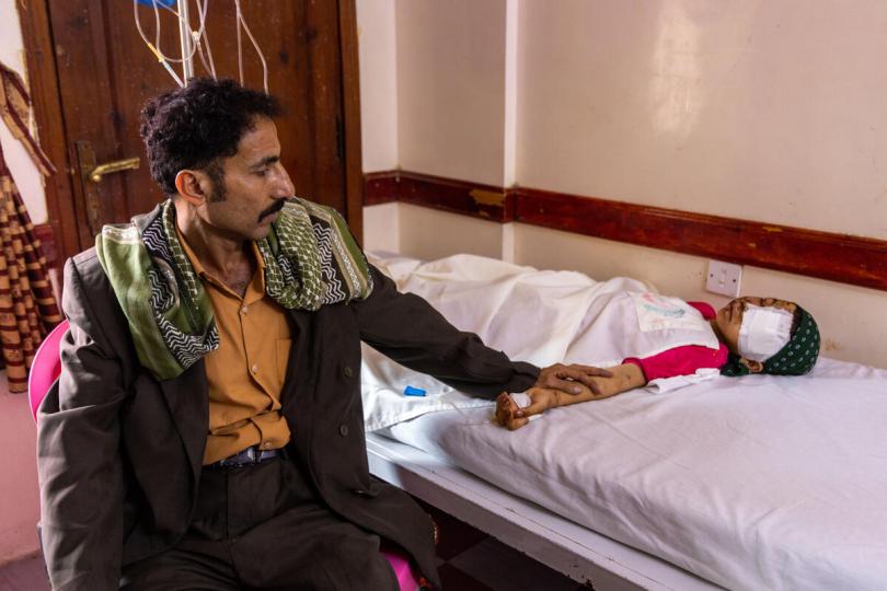 Jamal*, 38, sits in a hospital holding the hand of his 10-year-old daughter, Maha*, who was severely injured by a landmine in Taiz, Yemen