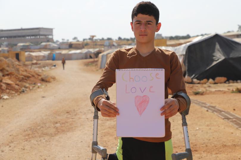Saleh* 15, wearing his crutches and holding a Choose Love drawing, Syria