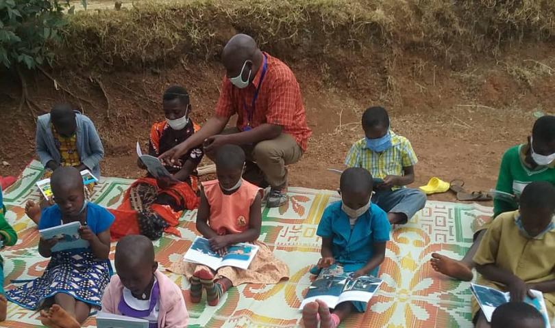 A community education worker supervising children during a free outdoor reading session, Rwanda