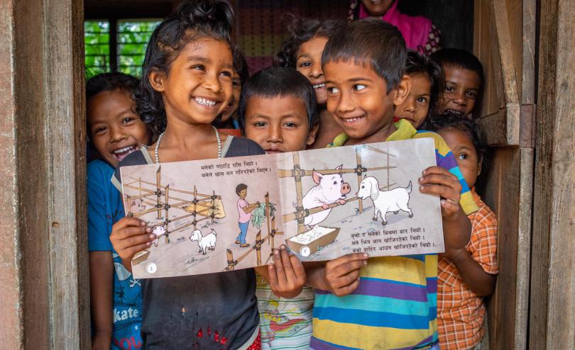Nepali children hold open an illustrated storybooks written in their local language of Maithili inside an early learning center.