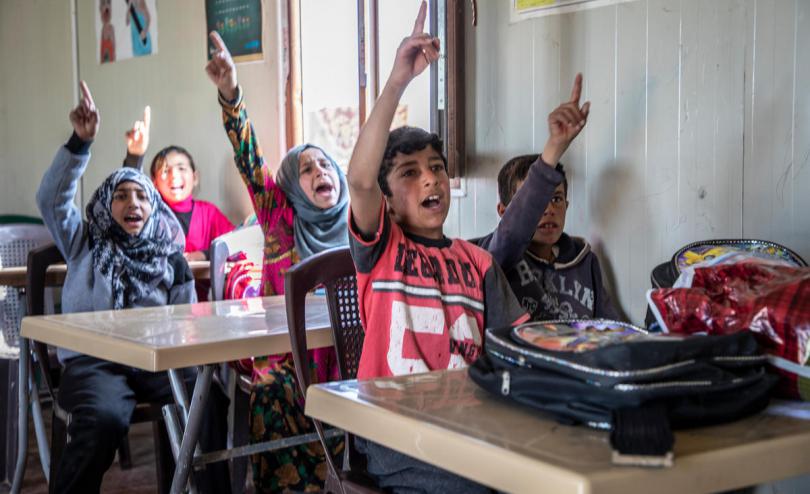 Children raise their hands in class in Syria