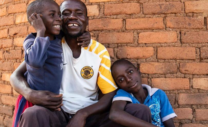 Ntokozo, 37 and his sons, smiling at the camera at their home in Zimbabwe
