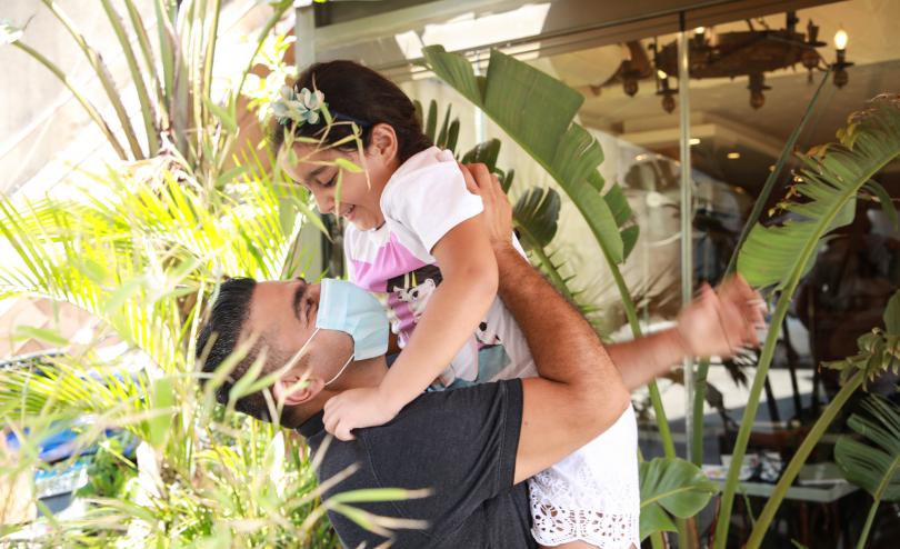 Sami* lifts up his daughter Layla*, 9, and hugs her in the garden of their home, surrounded by plants, in Beirut, Lebanon