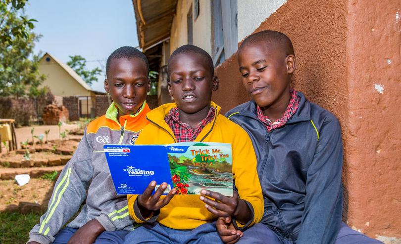 Ivan, Andre and Gerald take turn reading a book in Uganda.