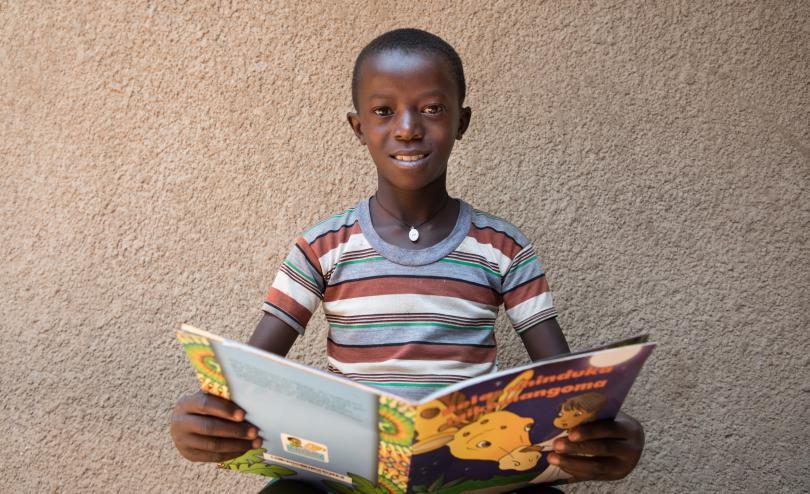 Wilson, 10, reading a book outside his reading club, Rwanda