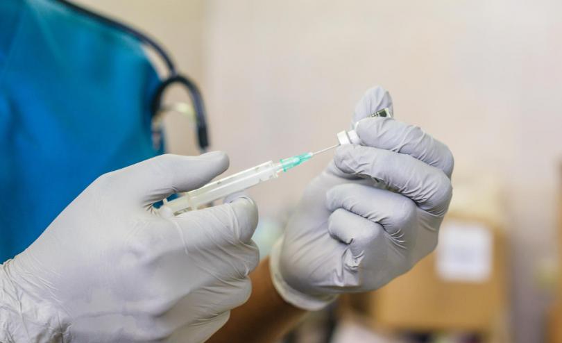 A person in white medical gloves prepares a vaccine in a needle