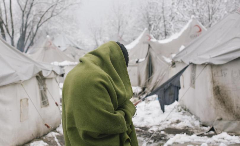 Refugee warming himself in blanket from sub zero temperatures at Vucjak camp / first snow of the year