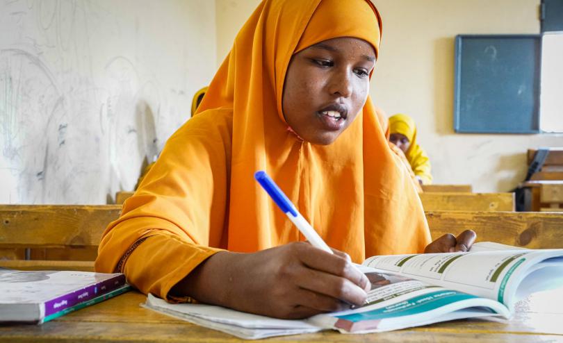 Farhiya, a 16 year old Somalian student wearing bright orange clothes, works at a schooldesk