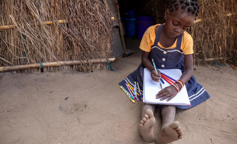 Clara*, 6, sits on the ground, writing.