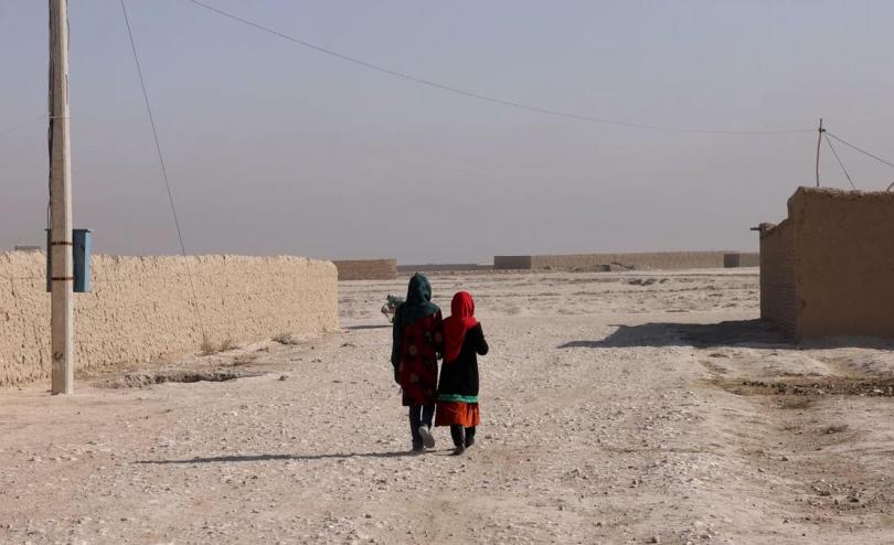 Two Afghan children walk down a street, photographed from behind