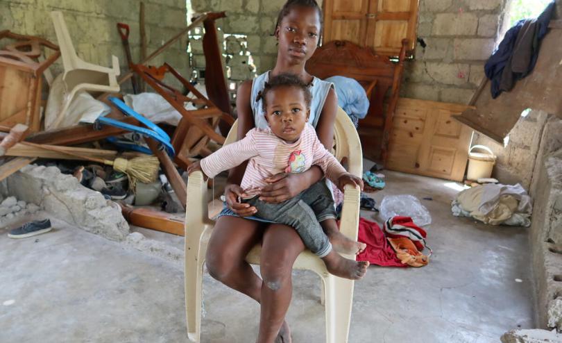 Nephtalie* (14) cradles her sister Gaelle* (18 months) on her lap in the remains of her destroyed house