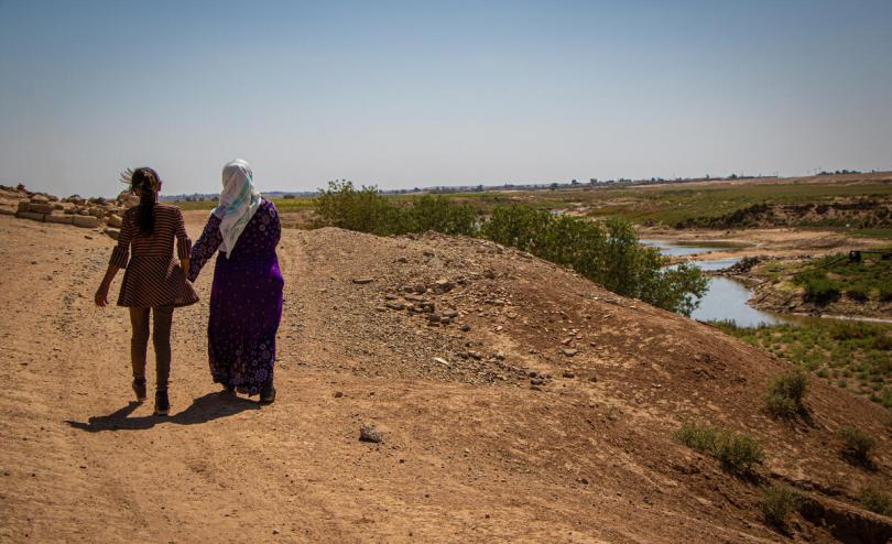 Bailasan*, 13, and her mother Maryam*, 50, walk by the river where drought has caused a water crisis in North East Syria