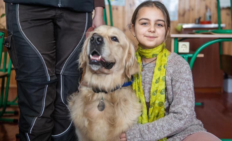 Viktoriya*, 9, poses with golden retriever Parker, a two-year-old therapy dog, during a dog therapy session at a school outside of Kyiv, Ukraine (Oleksandr Khomenko/Save the Children) 