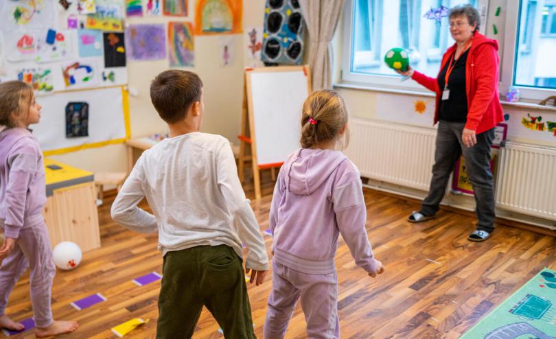 A Save the Children employee throws a ball to (from left to right) Maria*, 7, Symon*, 7 and Larissa*, 7 in the Child Friendly Space