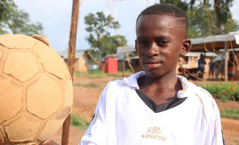 Samuel*, 13, holding his football in the settlement where his family lives in Ogoja, Nigeria