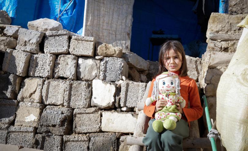 child outside ruined house with doll