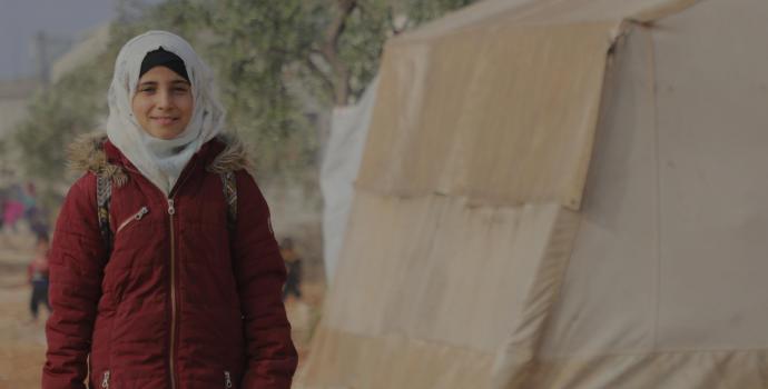 Marah standing in front of a tent on her way to school in Syria.