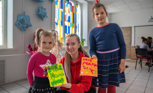 Olga Shults, Save the Children's programme manager, poses for portrait with *Marta (left) and *Lera (right) holding gift cards at Child Friendly Space in Mykolaiv, Ukraine