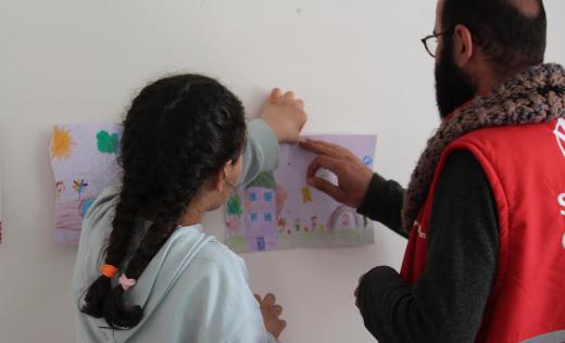 Eda*,10, hangs her drawing with Osman from Save the Children