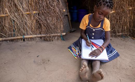 Clara*, 6, sits on the ground, writing.