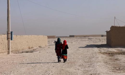 Two Afghan children walk down a street, photographed from behind