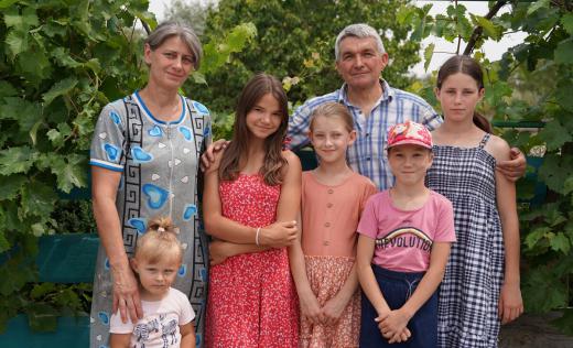 Stanislav*, 57, with his wife Oksana*, Anastasiia*(3), Mariia*(14), Victoria*(9), Larisa*(9), and Olga*(14) [left to right] pose for a family portrait in the garden near their house in Southern Dnipro, Ukraine