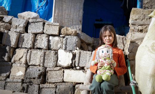 child outside ruined house with doll