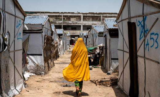 Miriam*, 16, walks past shelters in a camp for displaced people in Borno, Nigeria