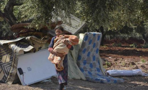 A young girl who has fled fighting in Idlib carries a baby in the temporary camp where she is staying