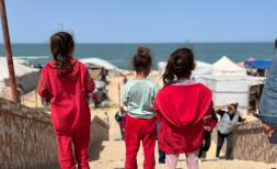 Three young girls dressed in red look out towards the sea in Rafah, Gaza