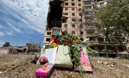 flowers and toys in front of bombed building